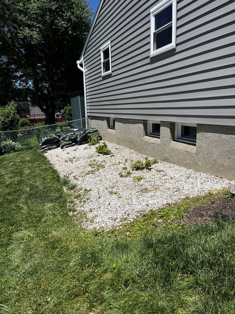 Before: an overgrown white-rock bed along a house foundation with weeds breaking through