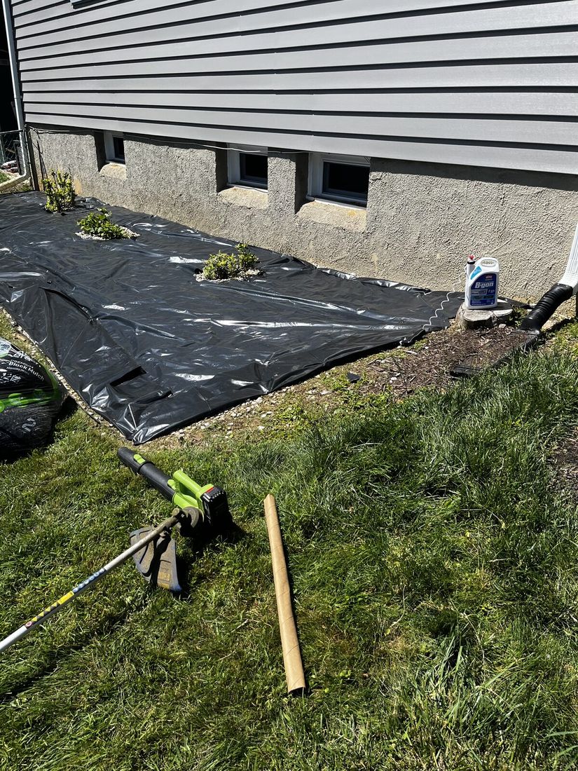 The cleared bed with black landscape fabric laid down along the foundation